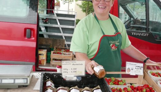 Verkäuferin auf Marktplatz mit Marmelade und Erdbeeren